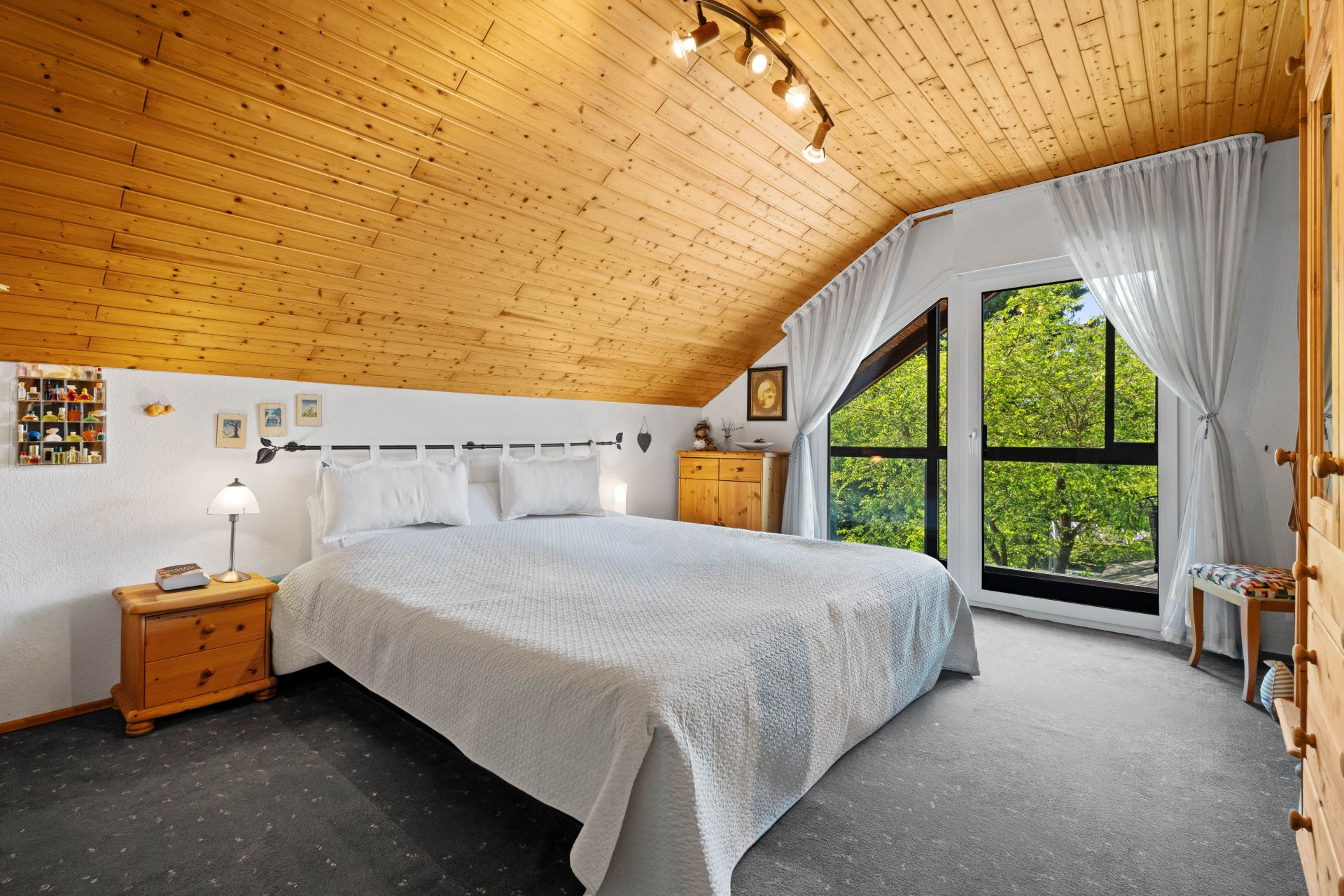 Helles Schlafzimmer mit Dachschräge, Doppelbett, Holzdecke und großem Fenster mit Blick ins Grüne.