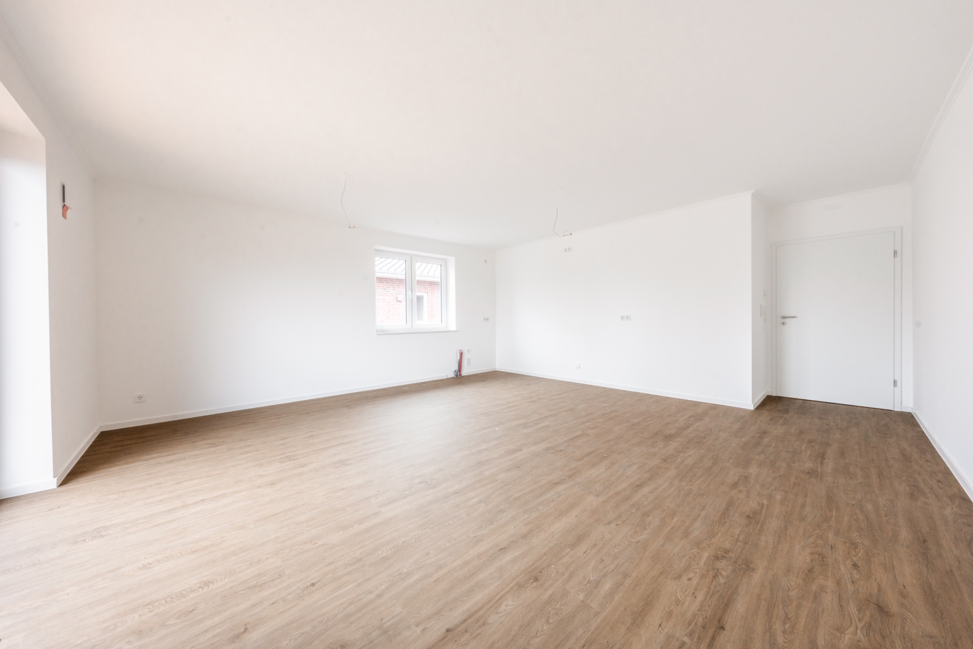 Heller, leerer Raum mit Holzfußboden, weißen Wänden, Fenster und Tür.