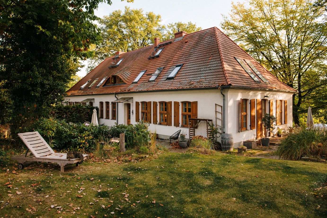 Großes weißes Haus mit rotem Dach, Holzfenstern und Garten im Grünen.