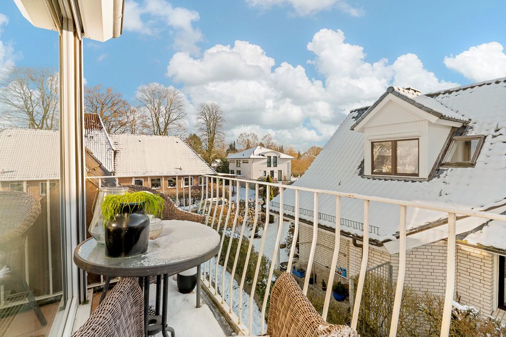 Kleiner Balkon mit Tisch, zwei Stühlen und Blick auf schneebedeckte Hausdächer.
