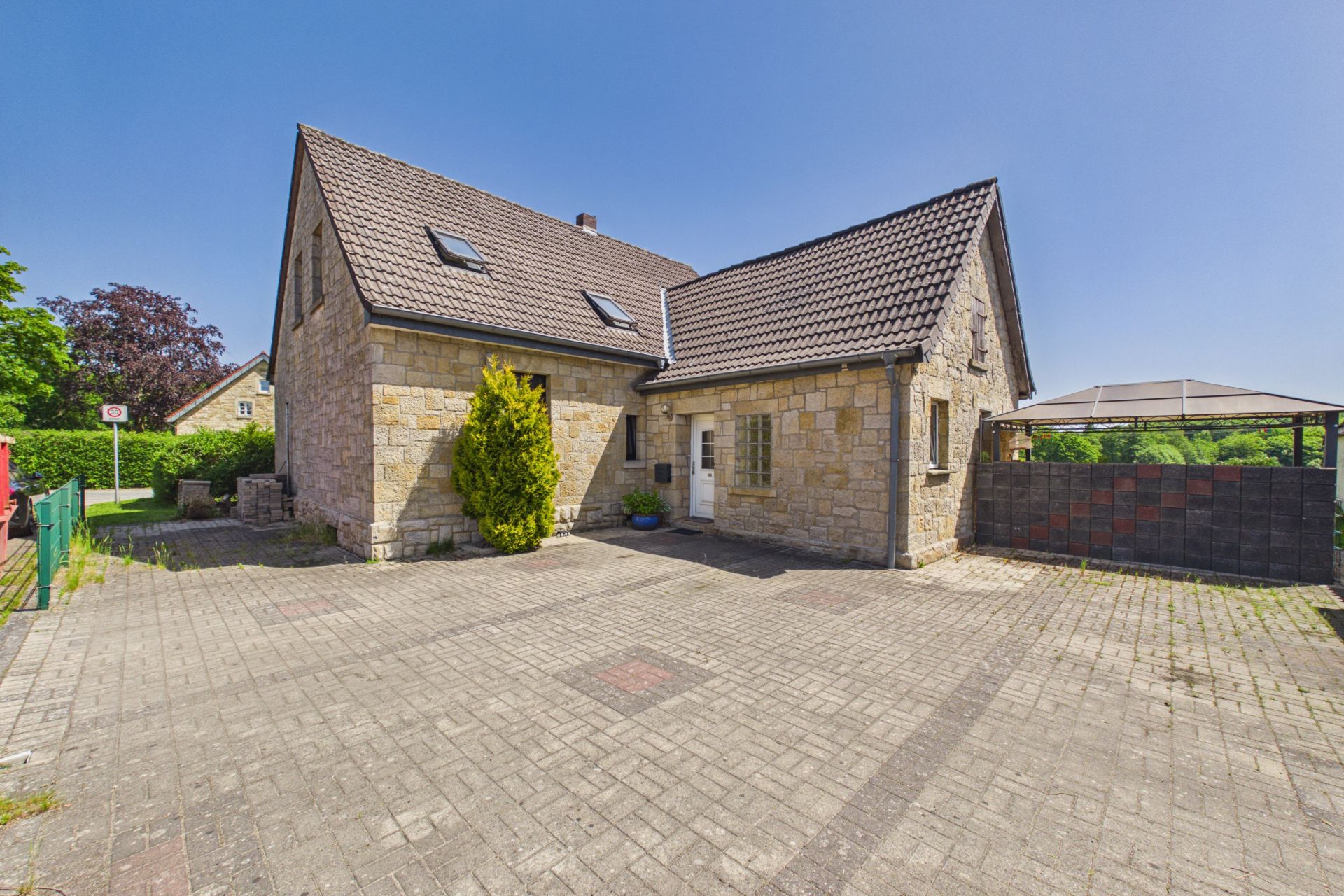 Steinhaus mit Satteldach, gepflasterter Hof und einem Baum vor dem Eingang.