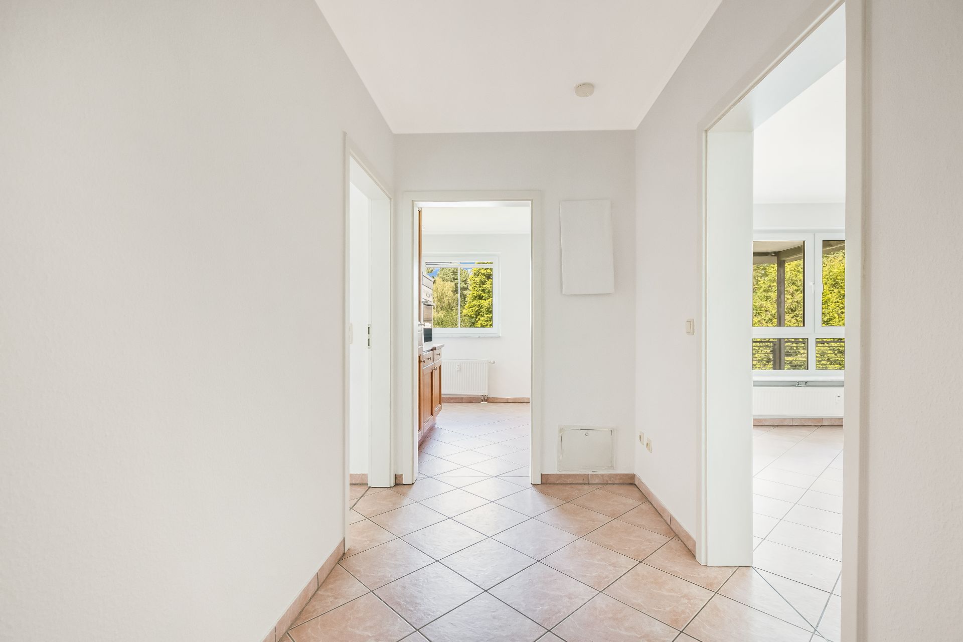 Heller Flur mit gefliestem Boden, Türen führen zu Küche und Wohnzimmer mit großen Fenstern.
