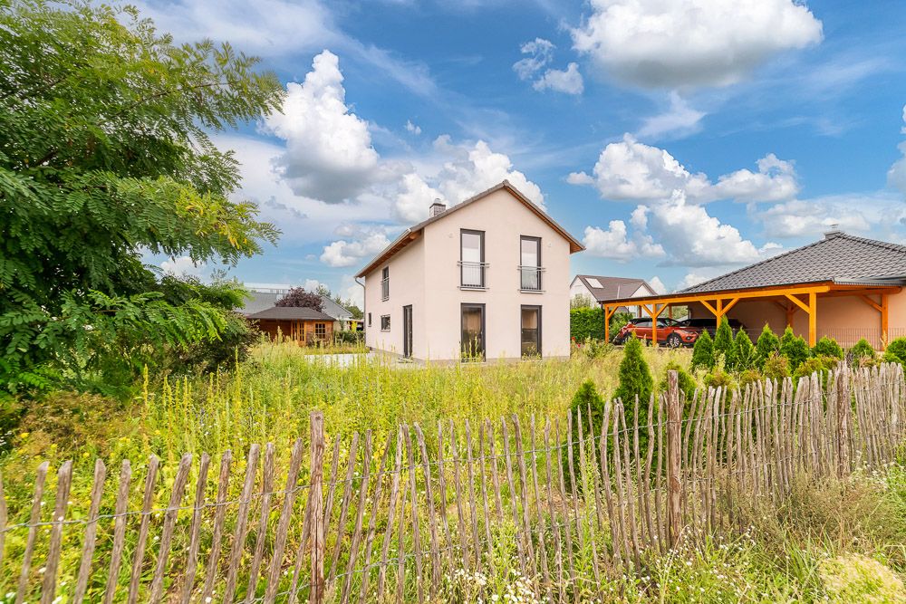 Modernes, zweistöckiges Haus mit großem Garten und Holzzaun im Vordergrund.