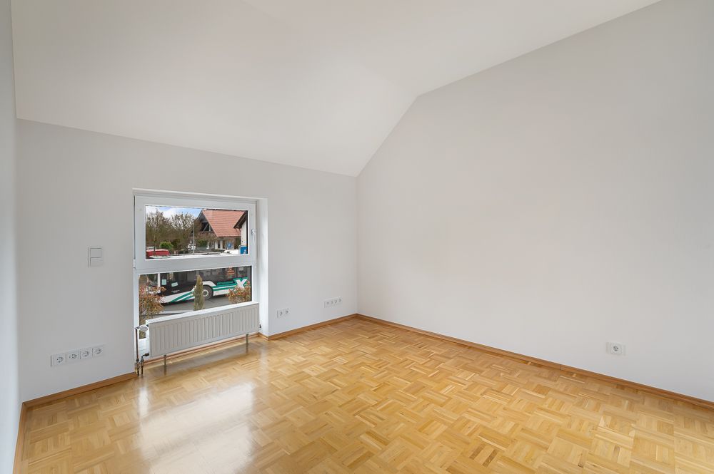 Leerer Raum mit hellem Parkettboden und großem Fenster, weiße Wände, Dachschräge.