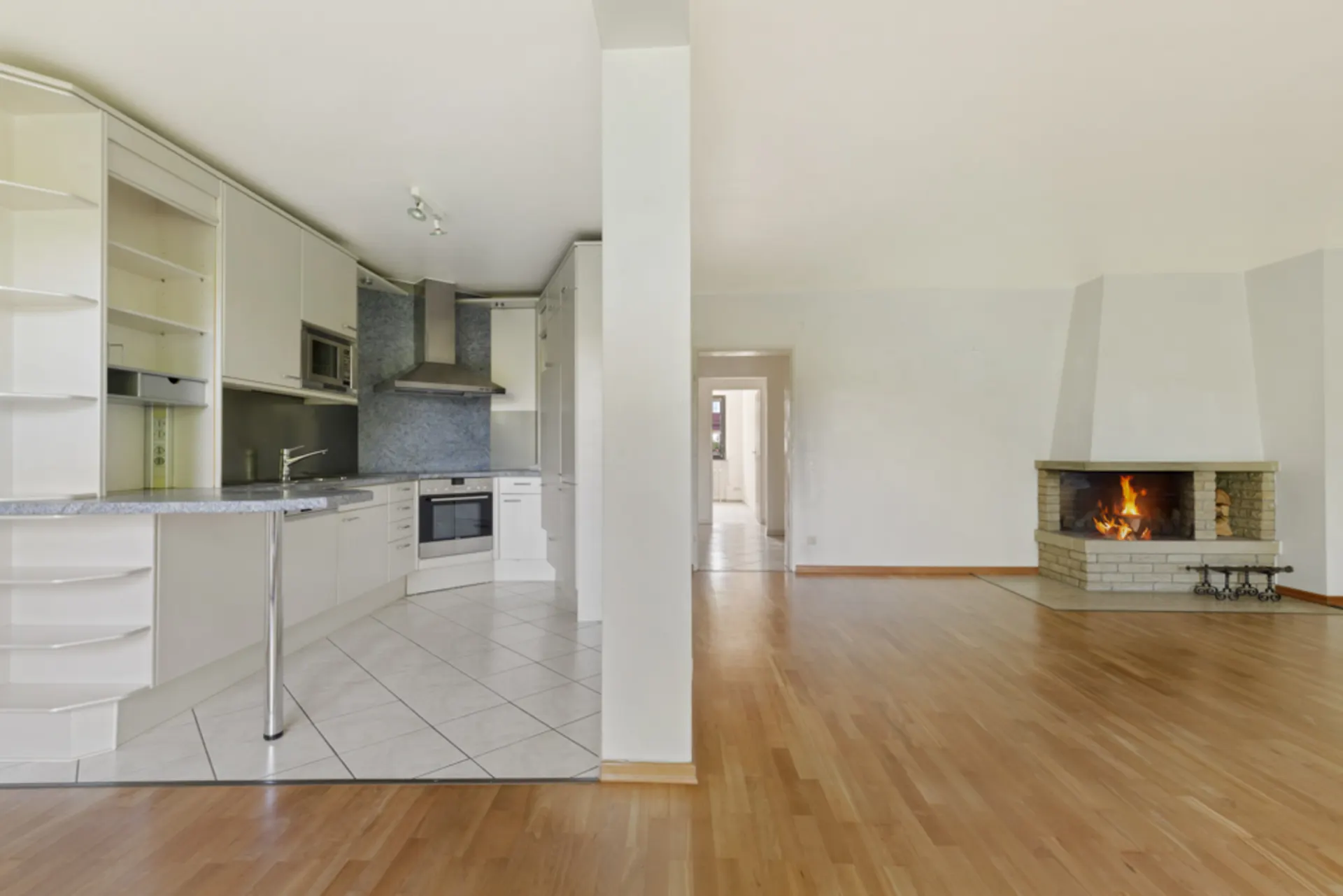 Offene Küche mit weißen Schränken und angrenzendem Wohnzimmer mit Kamin und Parkettboden.
