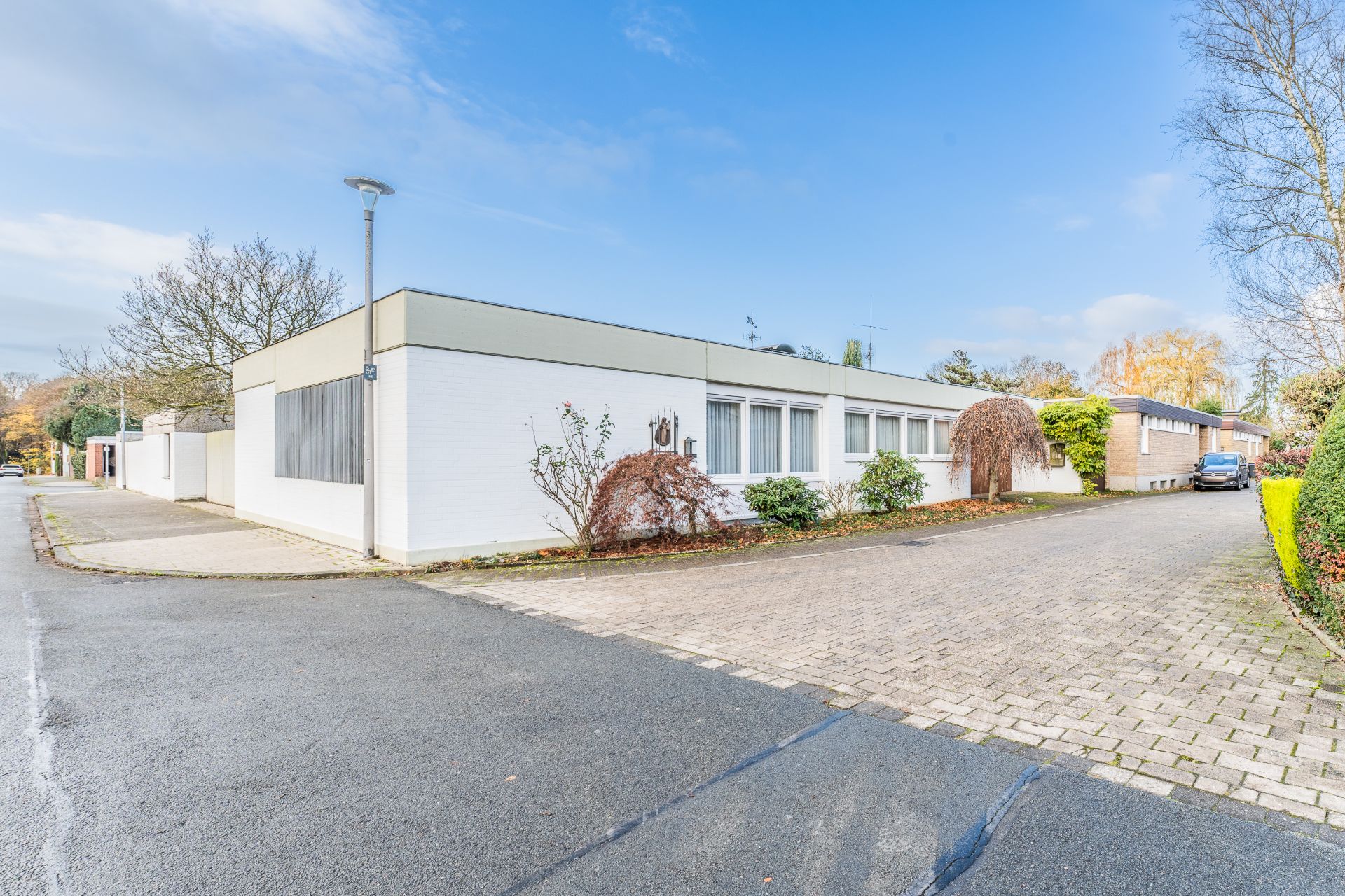 Einfamilienhaus mit flachem Dach, weißen Wänden und Vorgarten an einer ruhigen Straße.