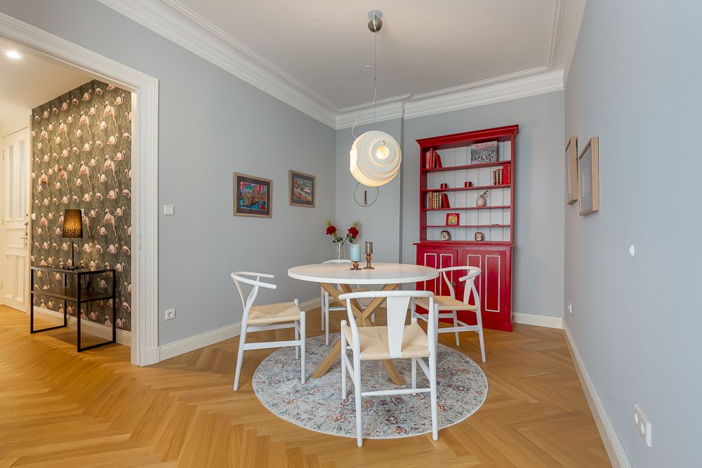 Essbereich mit rundem Tisch, vier weißen Stühlen und rotem Regal auf Holzfußboden.