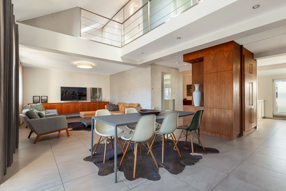 Modernes Wohnzimmer mit Esstisch, Stühlen und offener Galerie, helle Fliesen und Holzmöbel.