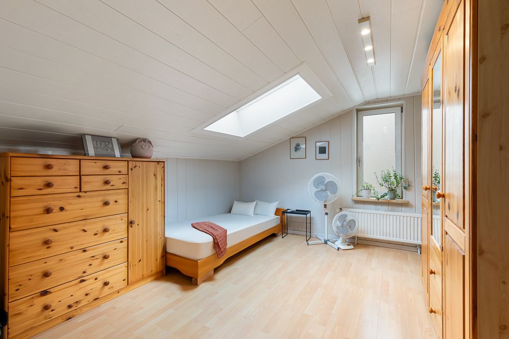 Helles Schlafzimmer mit Einzelbett, Holzschränken und Dachfenster.