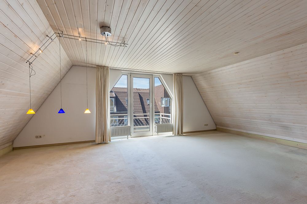 Helles Dachzimmer mit Holzdecke, drei bunten Hängelampen und Balkonzugang durch Glastüren.