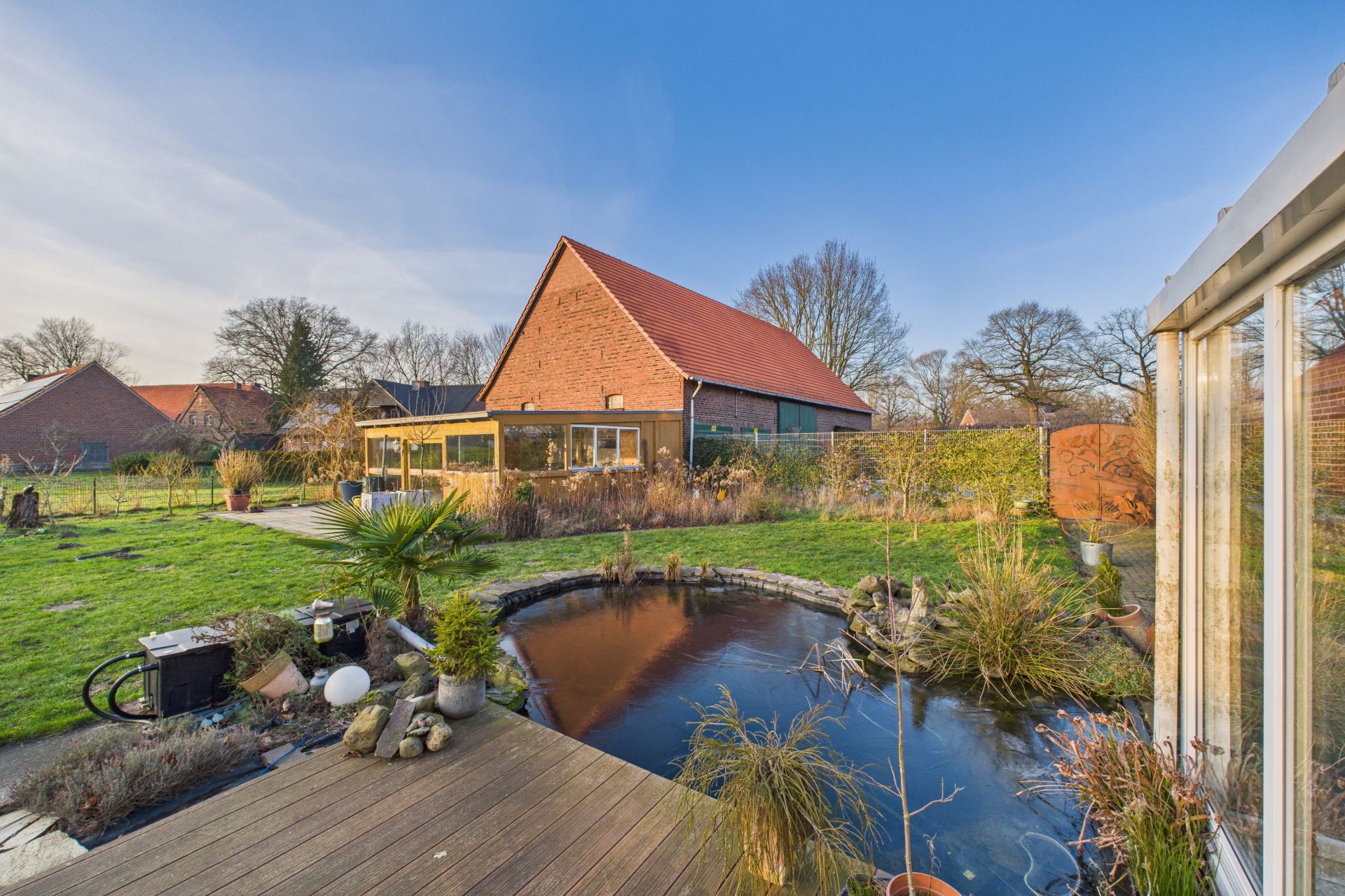 Garten mit kleinem Teich, Terrasse und Blick auf ein Haus mit rotem Dach.