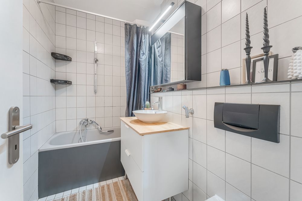 Modernes Badezimmer mit Badewanne, Waschbecken, Spiegel und grauen Fliesen.