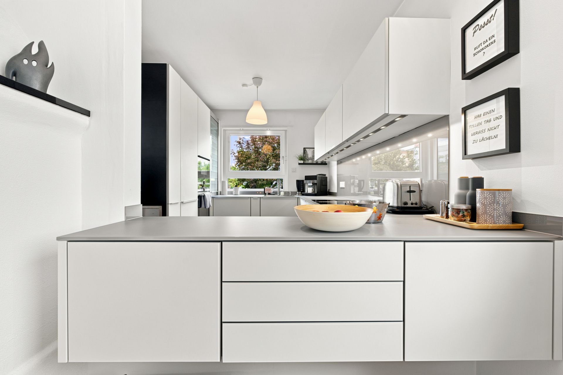 Moderne weiße Küche mit Schränken, Arbeitsplatte, Obstschale und Küchengeräten.