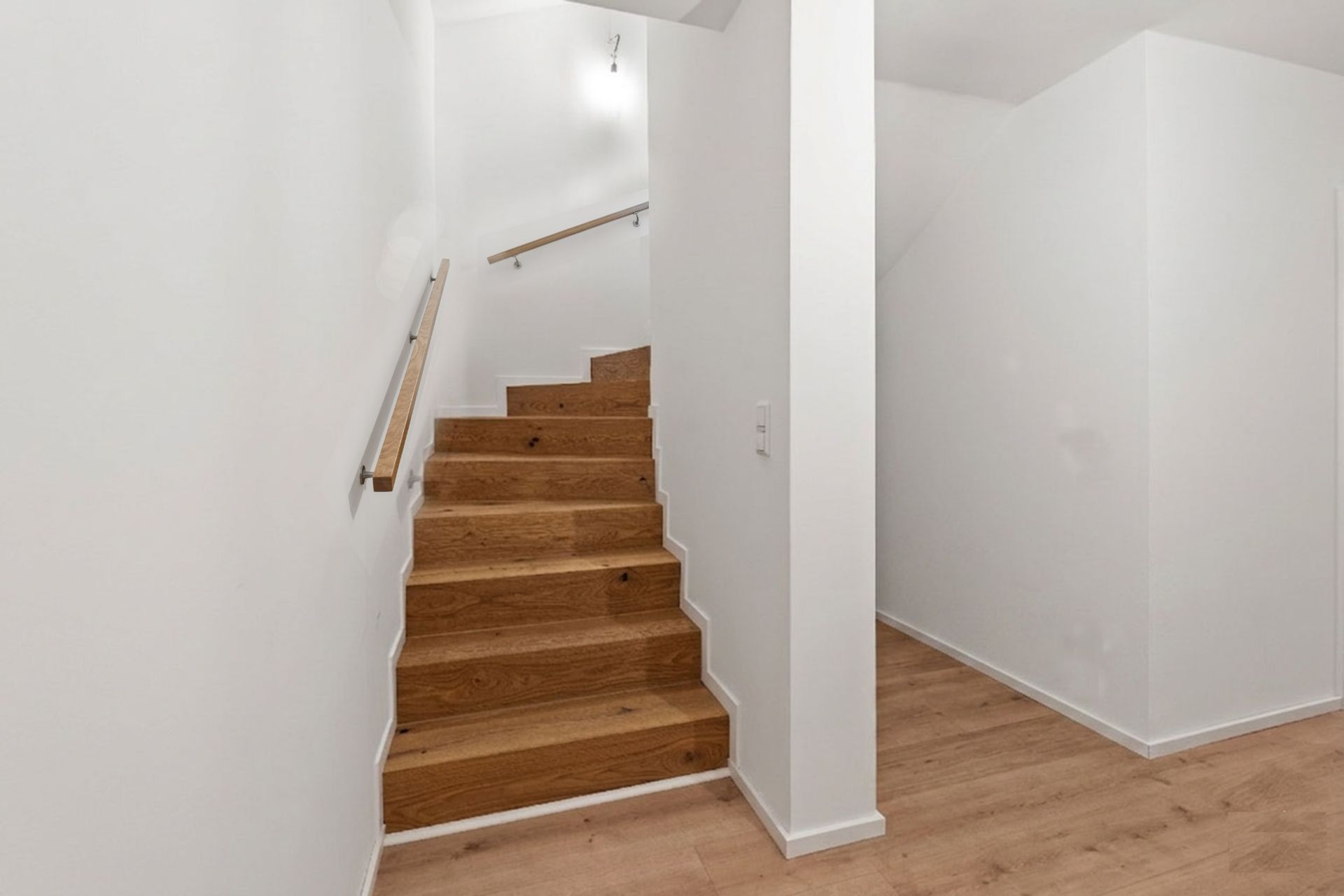 Hölzerne Treppe mit Handlauf in einem hellen Flur mit weißen Wänden.