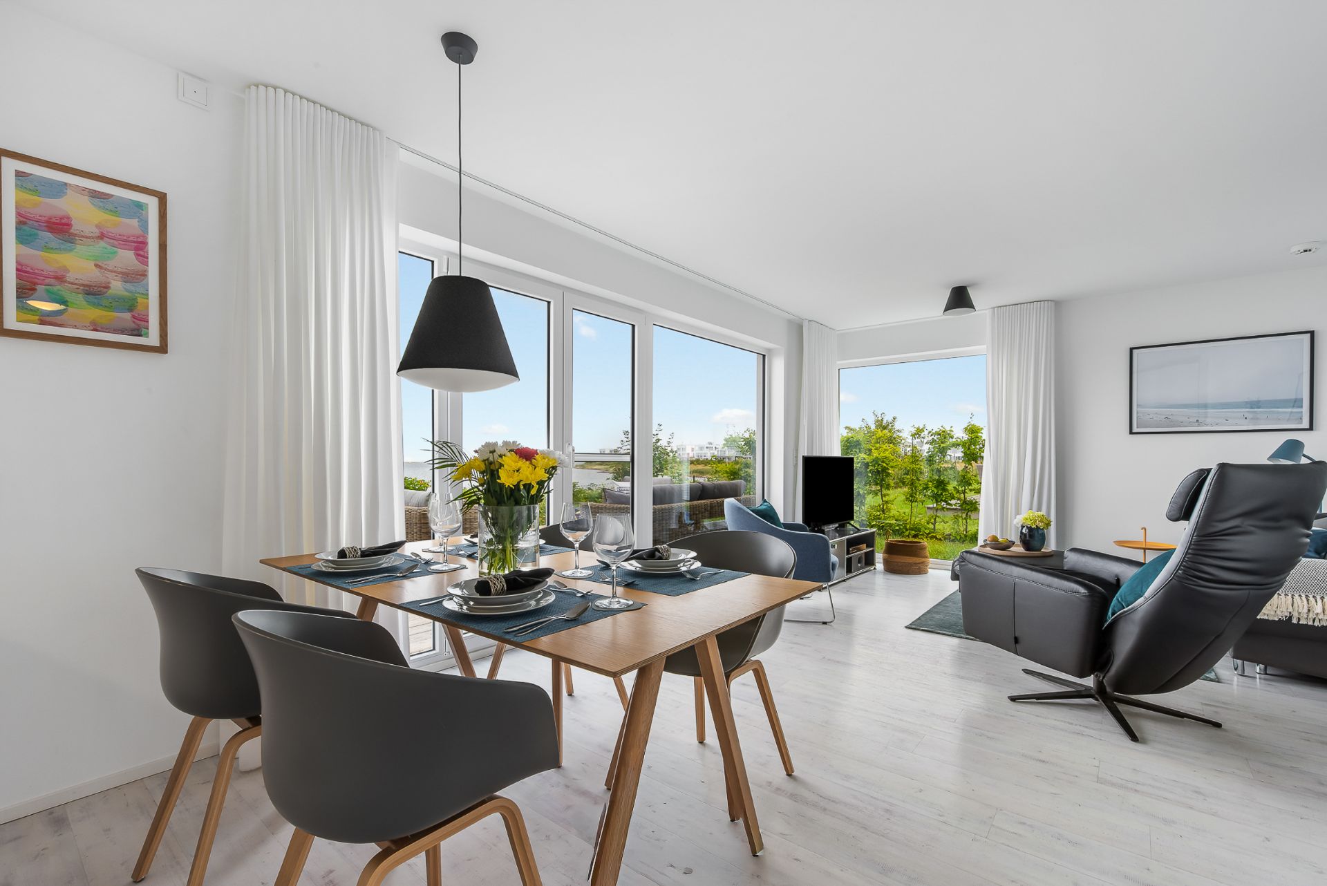 Helles Wohnzimmer mit Essbereich, großen Fenstern, modernen Stühlen und einem Sofa.