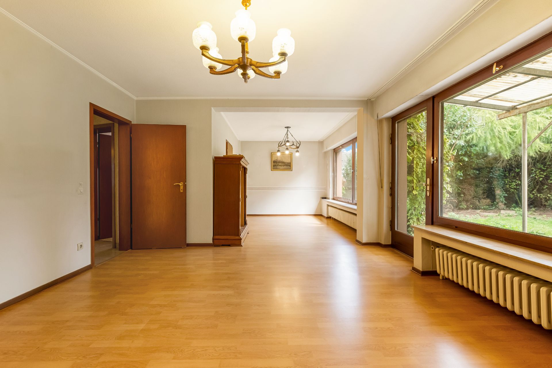 Großer, heller Raum mit Parkettboden, großen Fenstern, Deckenleuchten und Holztüren.