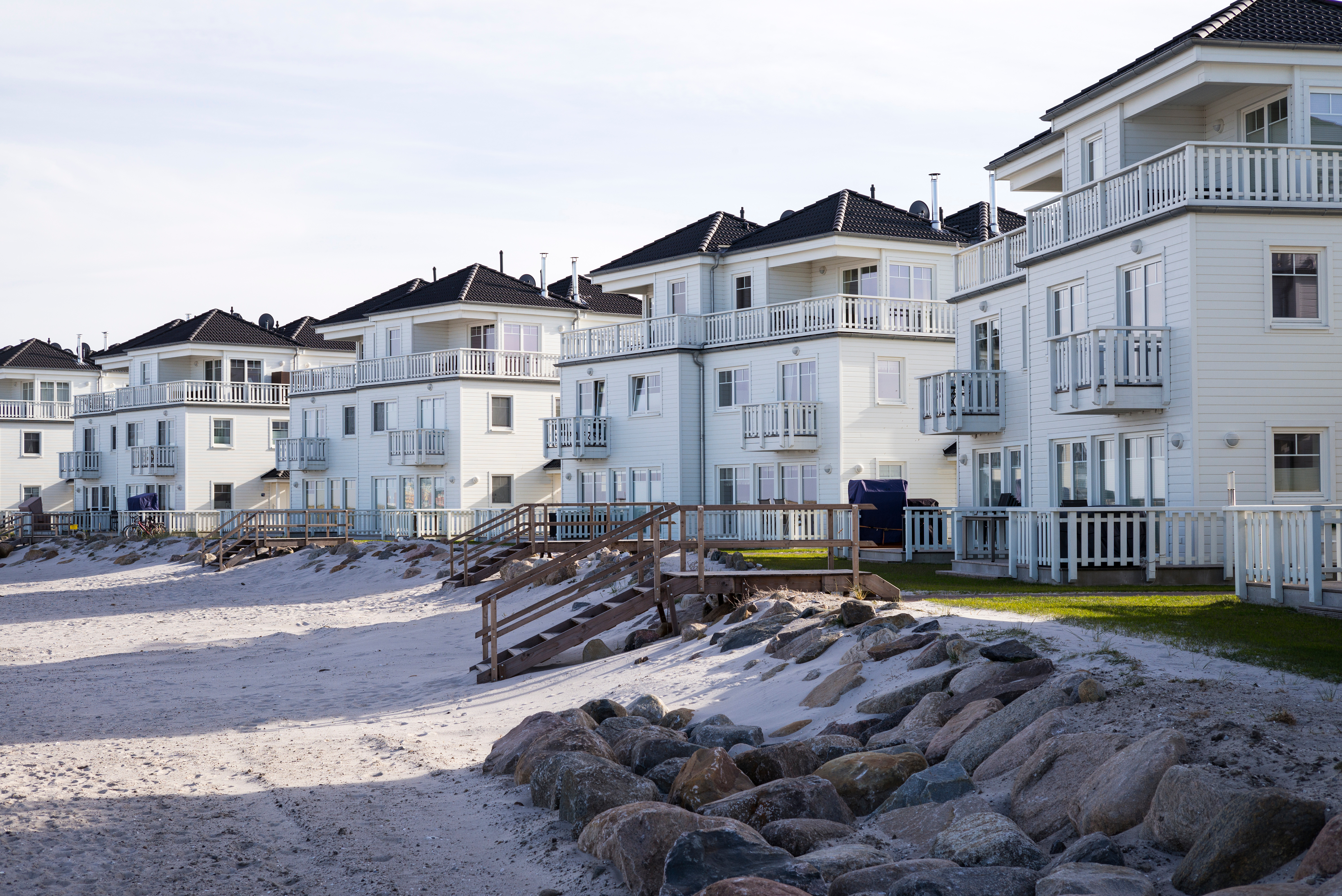 Moderne, mehrstöckige Wohnhäuser am Strand mit Holzzäunen und Balkonen.