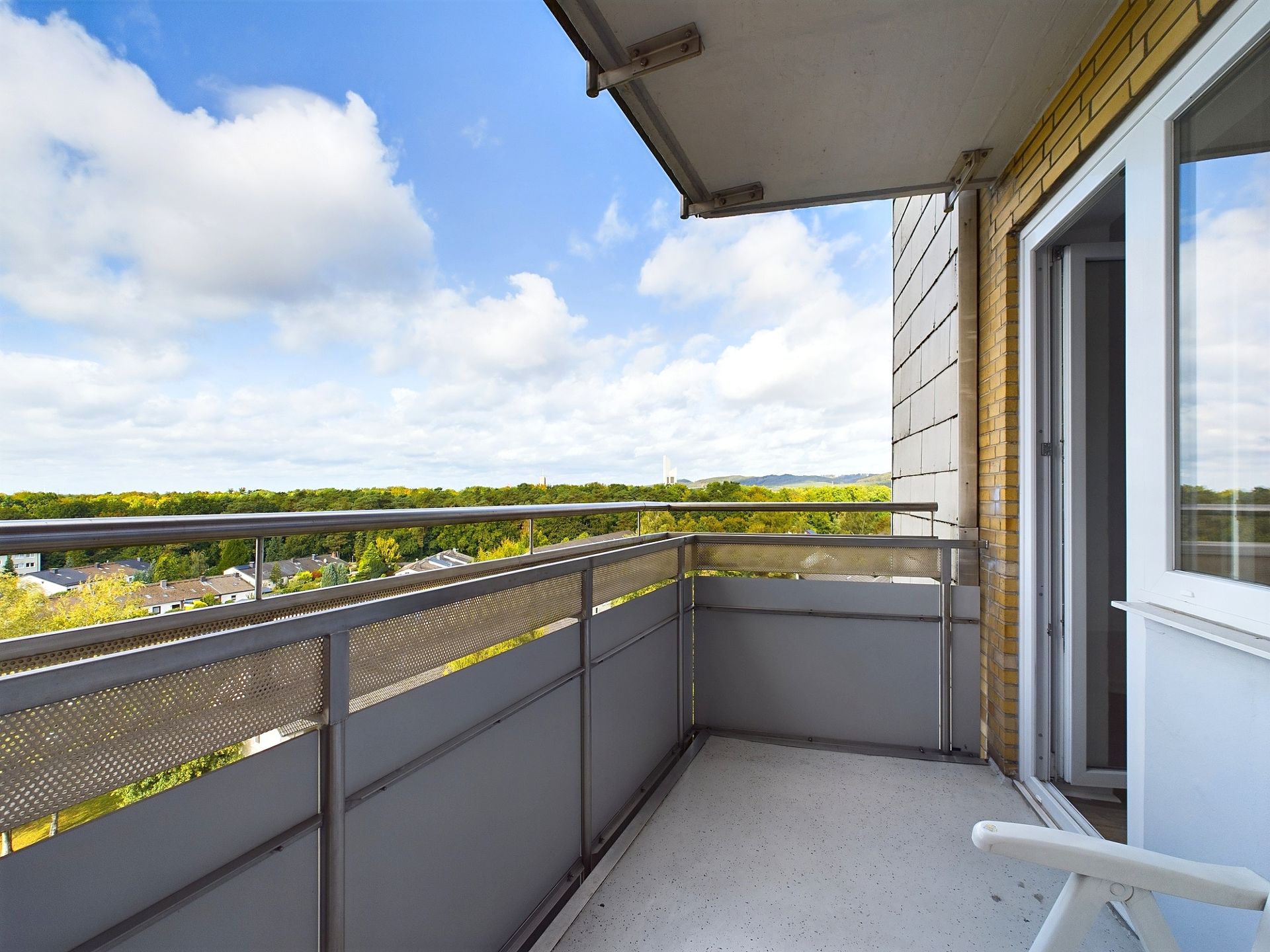 Balkon mit Geländer, Ausblick auf grüne Bäume und ein geöffnetes Fenster.