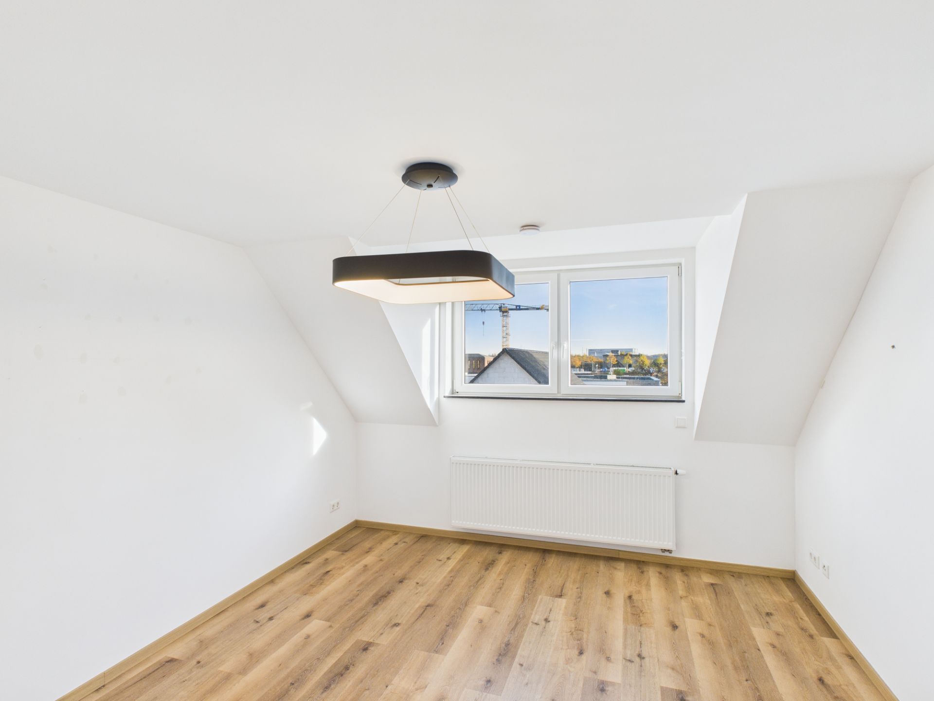 Helles Zimmer mit Holzfußboden, Dachfenster und moderner Deckenlampe.