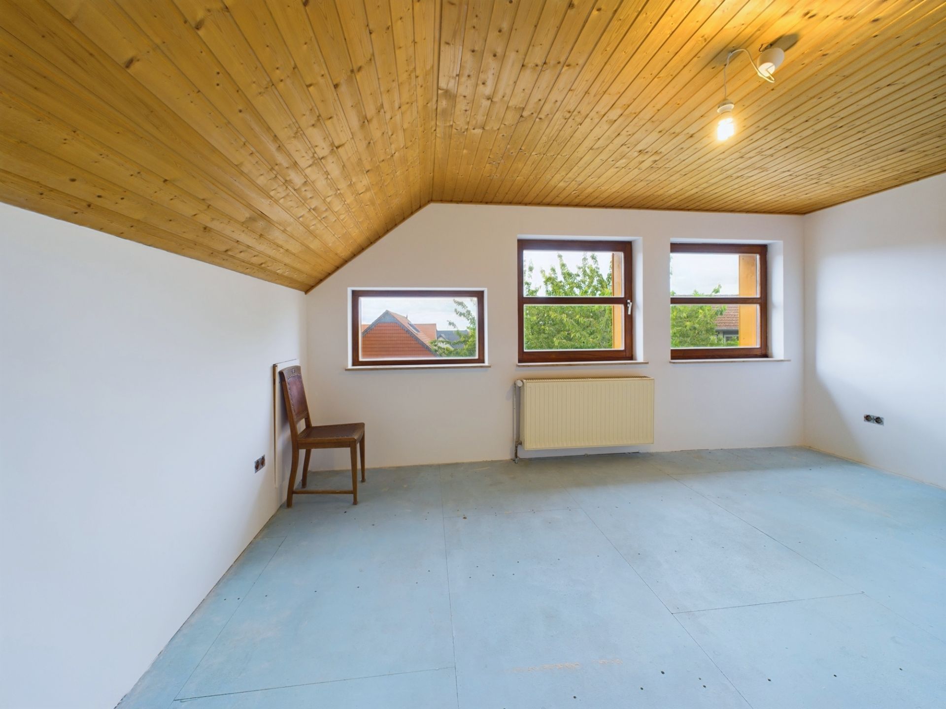 Leerer Raum mit Holzdecke, drei Fenstern und einem Stuhl an der Wand.