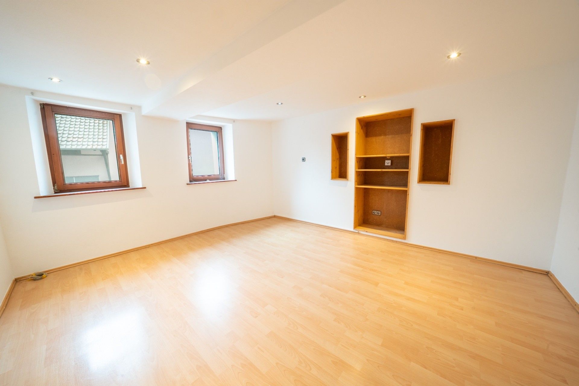 Heller Raum mit Holzfußboden, zwei Fenstern und eingebauten Wandregalen.
