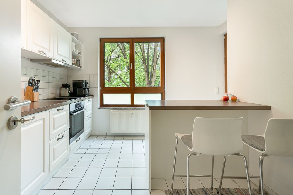 Moderne helle Küche mit Einbaumöbeln, Fenster, Tresen und zwei weißen Stühlen.