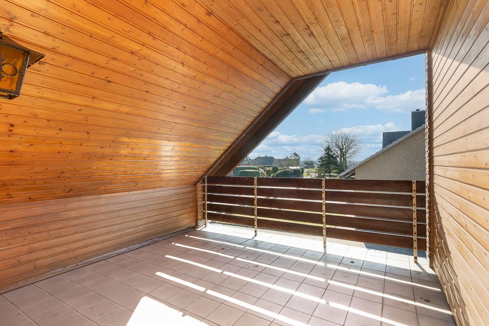 Überdachter Balkon mit Holzverkleidung und Blick auf Nachbarhäuser, Himmel und Bäume.