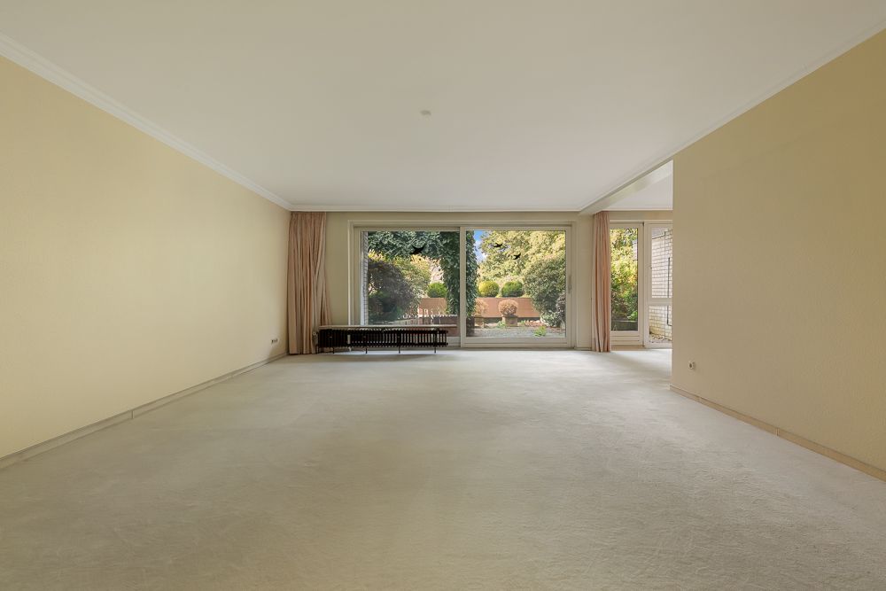 Leerer, heller Raum mit großen Fenstern und Blick auf einen Garten.