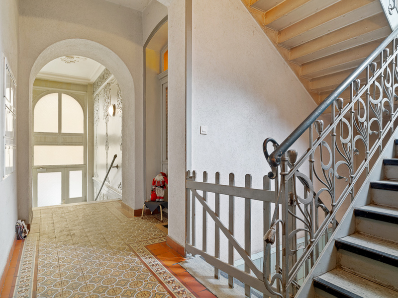Heller Hausflur mit gemustertem Boden, Treppe und verzierten Geländern.