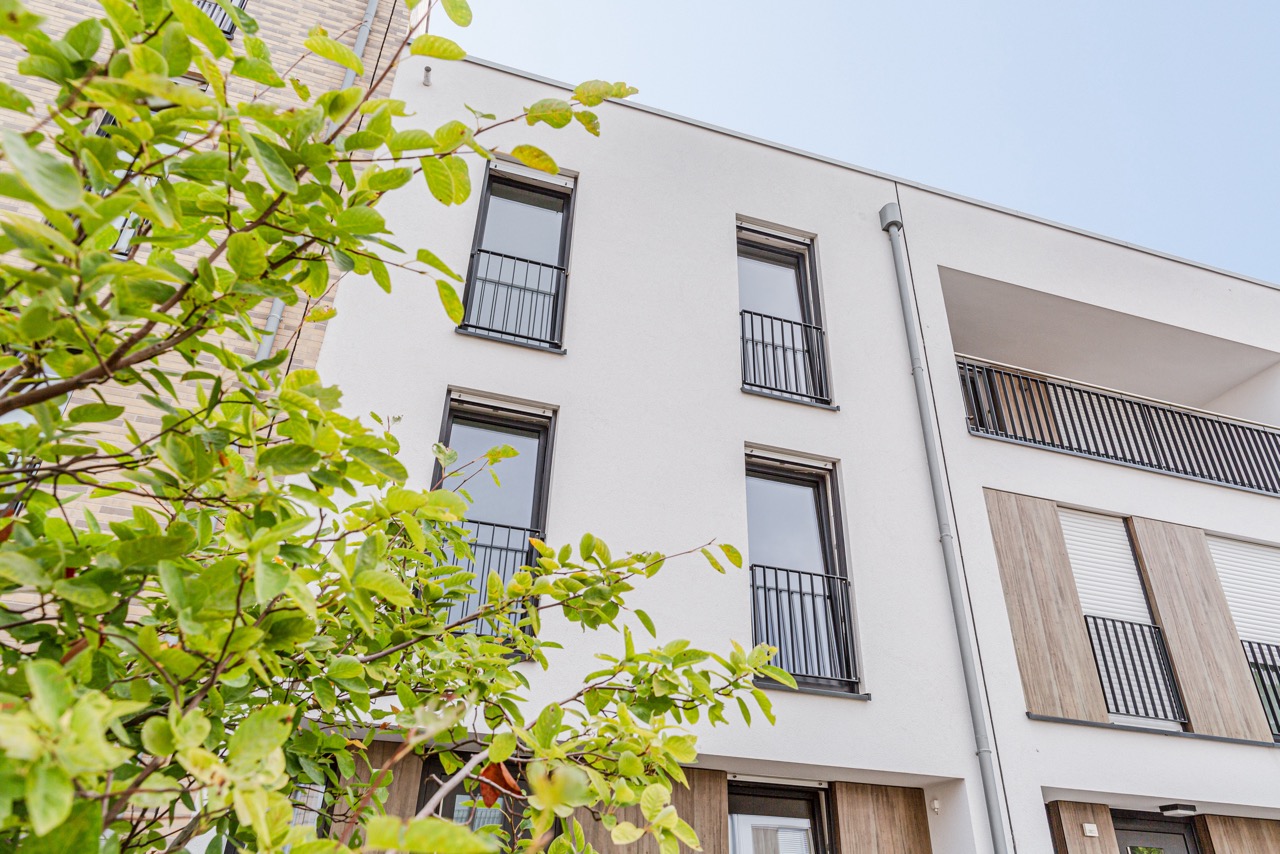 Fassade eines modernen Wohngebäudes mit großen Fenstern und einem Baum im Vordergrund.