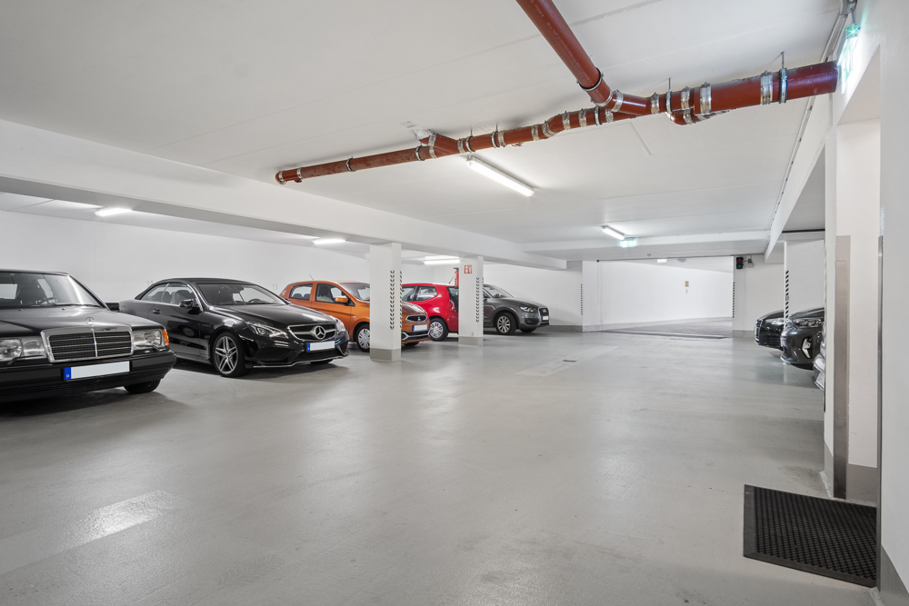 Helle Tiefgarage mit geparkten Autos und sichtbaren roten Rohrleitungen an der Decke.