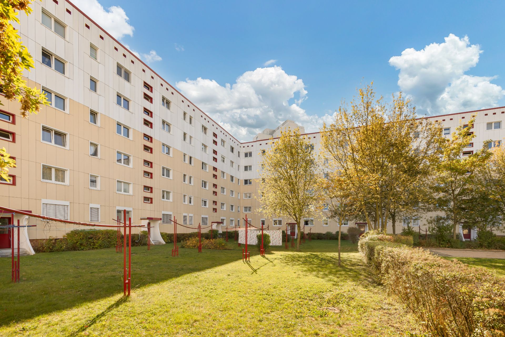 Innenhof einer Wohnanlage mit Rasen, Bäumen und Volleyballnetz vor mehrstöckigem Gebäude.