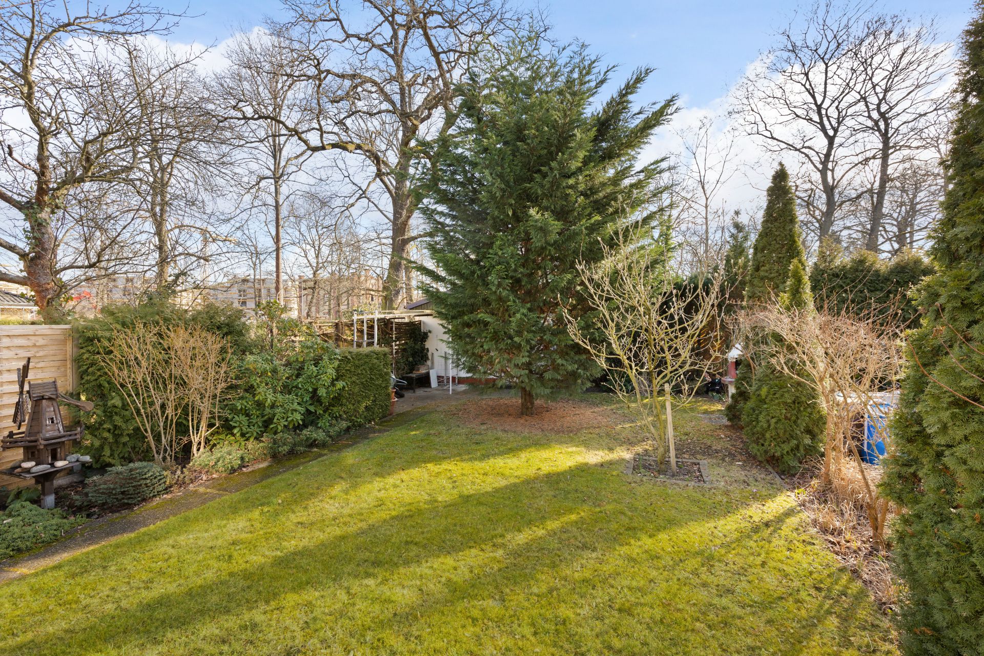 Grüner Garten mit Rasen, Büschen und Bäumen, im Hintergrund ein kleiner Schuppen.