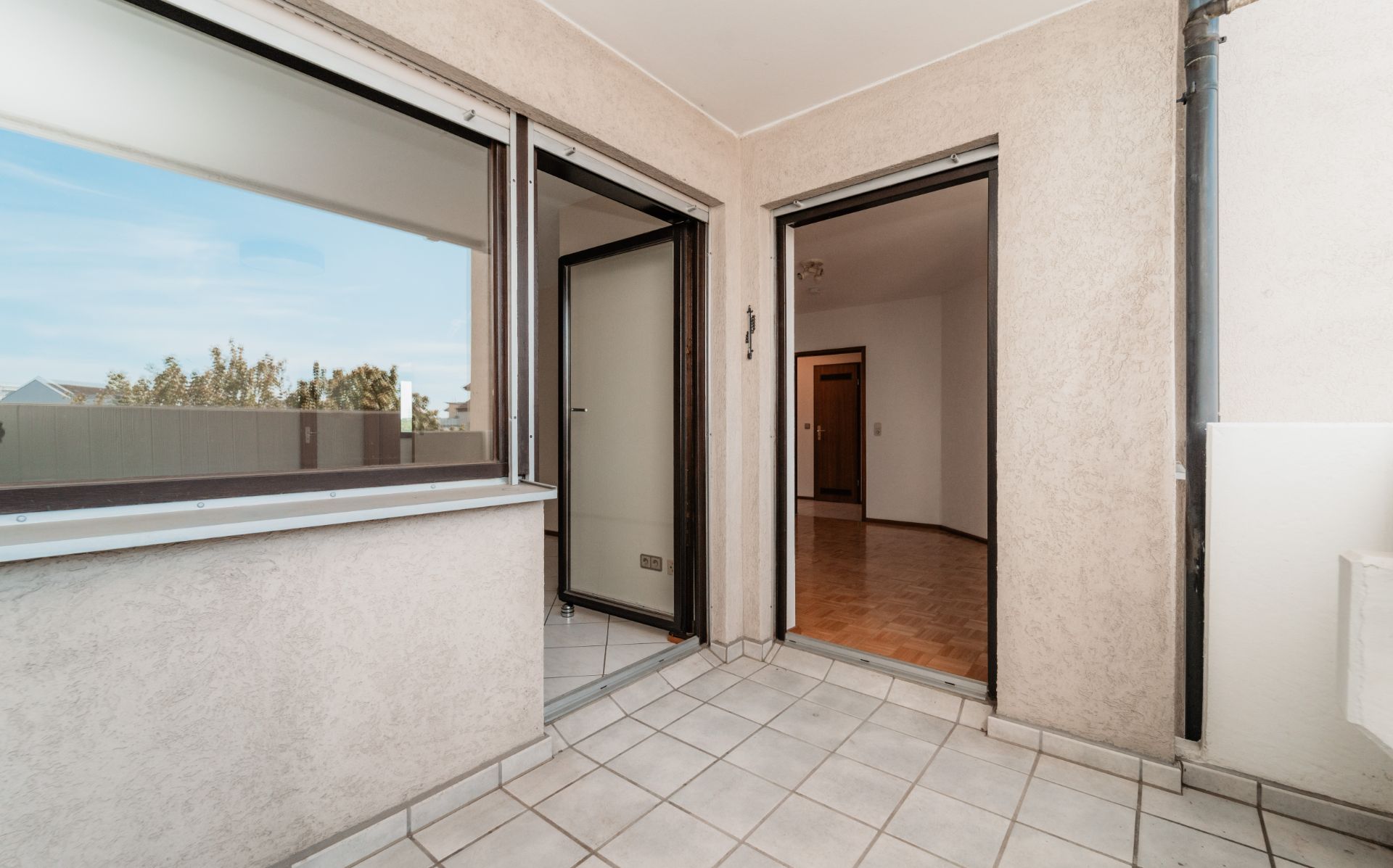 Überdachter Balkon mit Fliesenboden und Zugang zu einem Zimmer mit Holzboden.