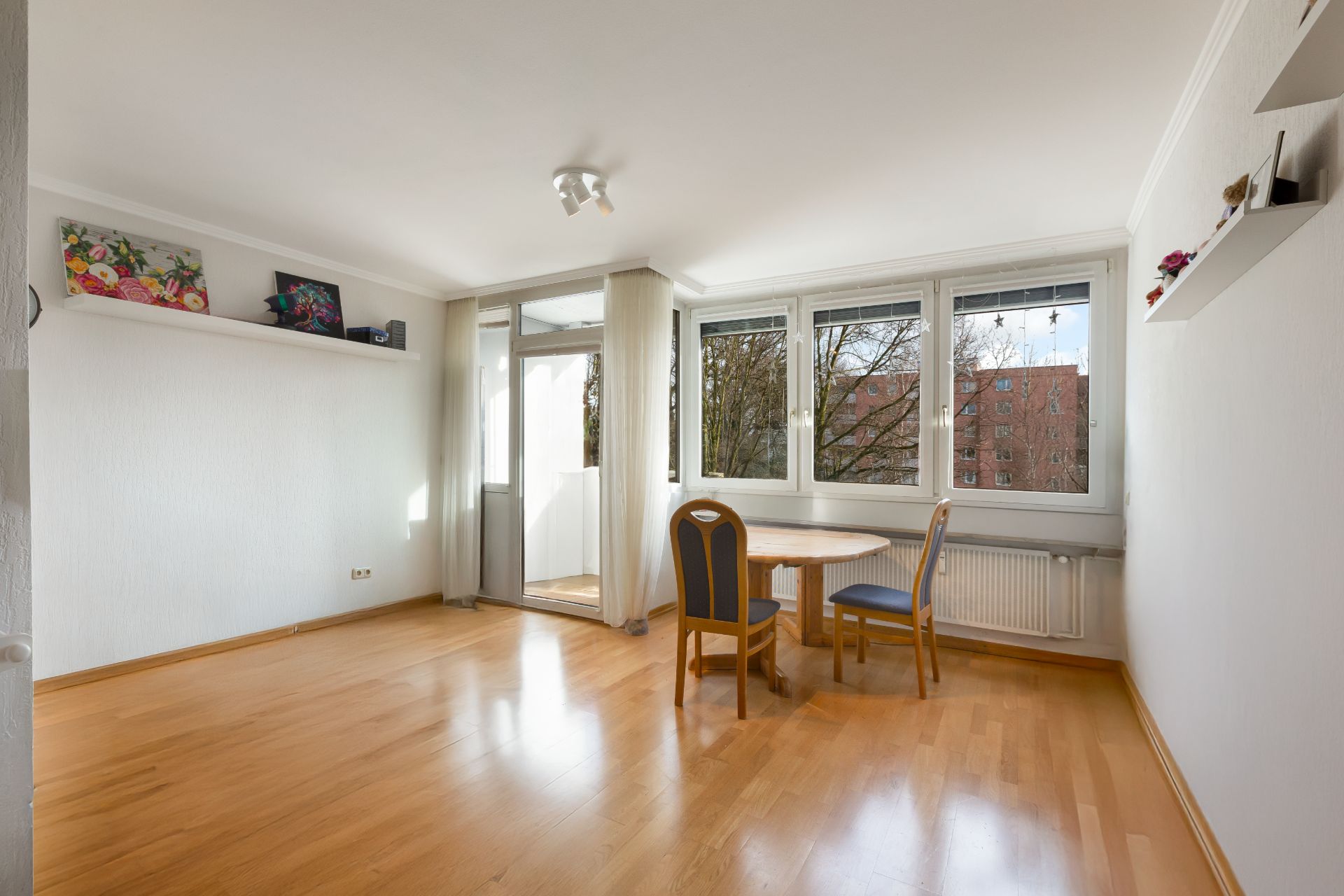 Helles Wohnzimmer mit Holzboden, Esstisch, zwei Stühlen und großen Fenstern.