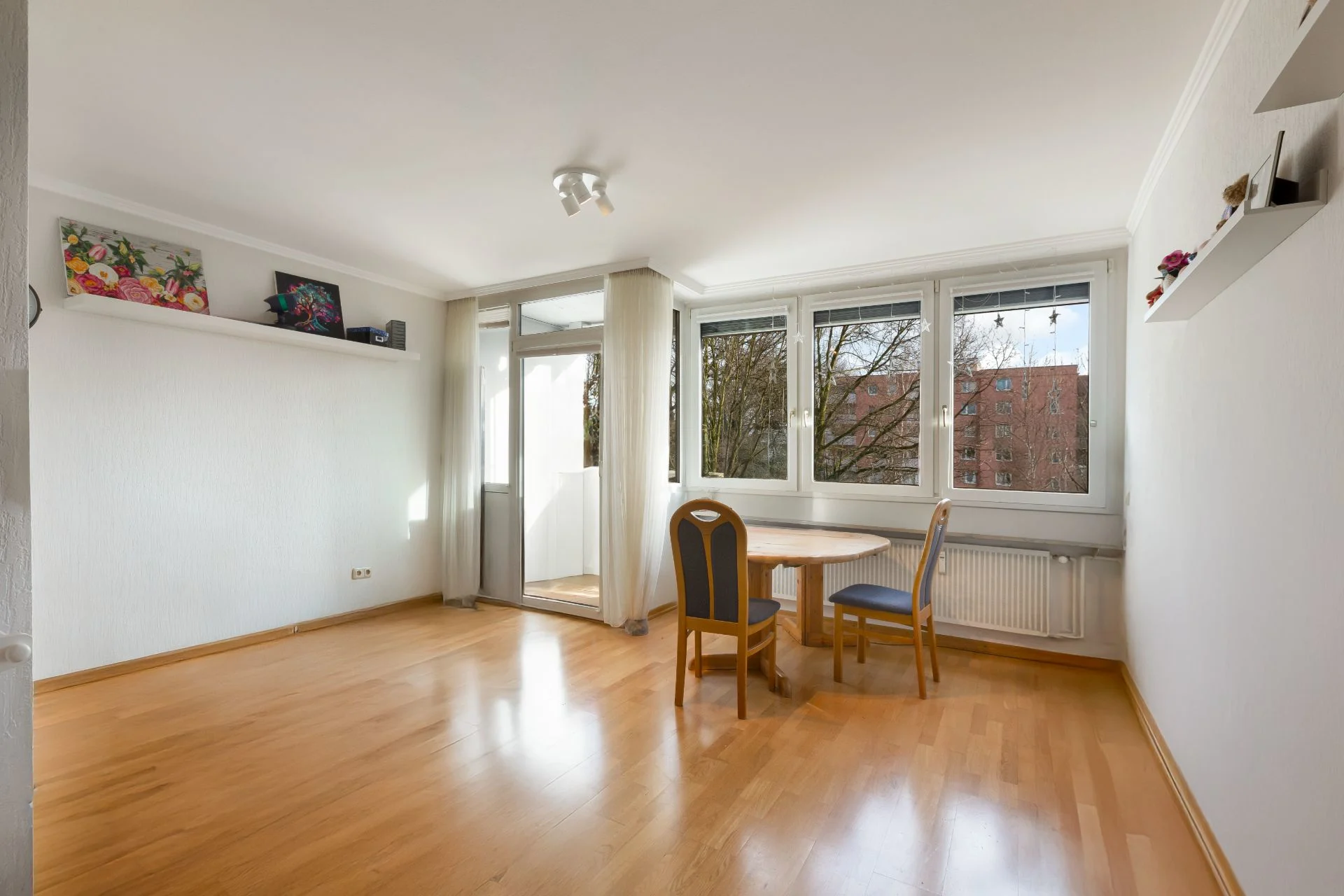 Helles Wohnzimmer mit Holzboden, Esstisch, zwei Stühlen und großen Fenstern.