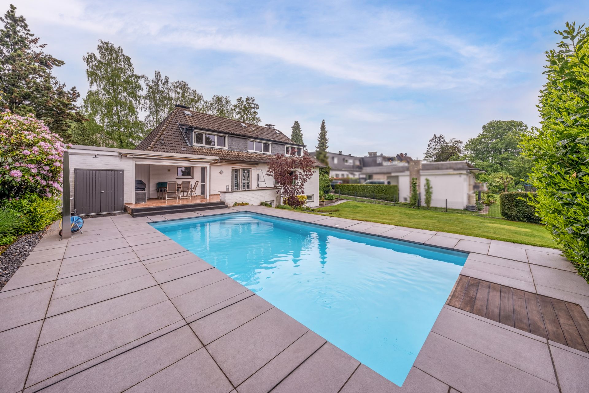 Gepflegter Garten mit großem Pool und einer Terrasse an einem Einfamilienhaus.