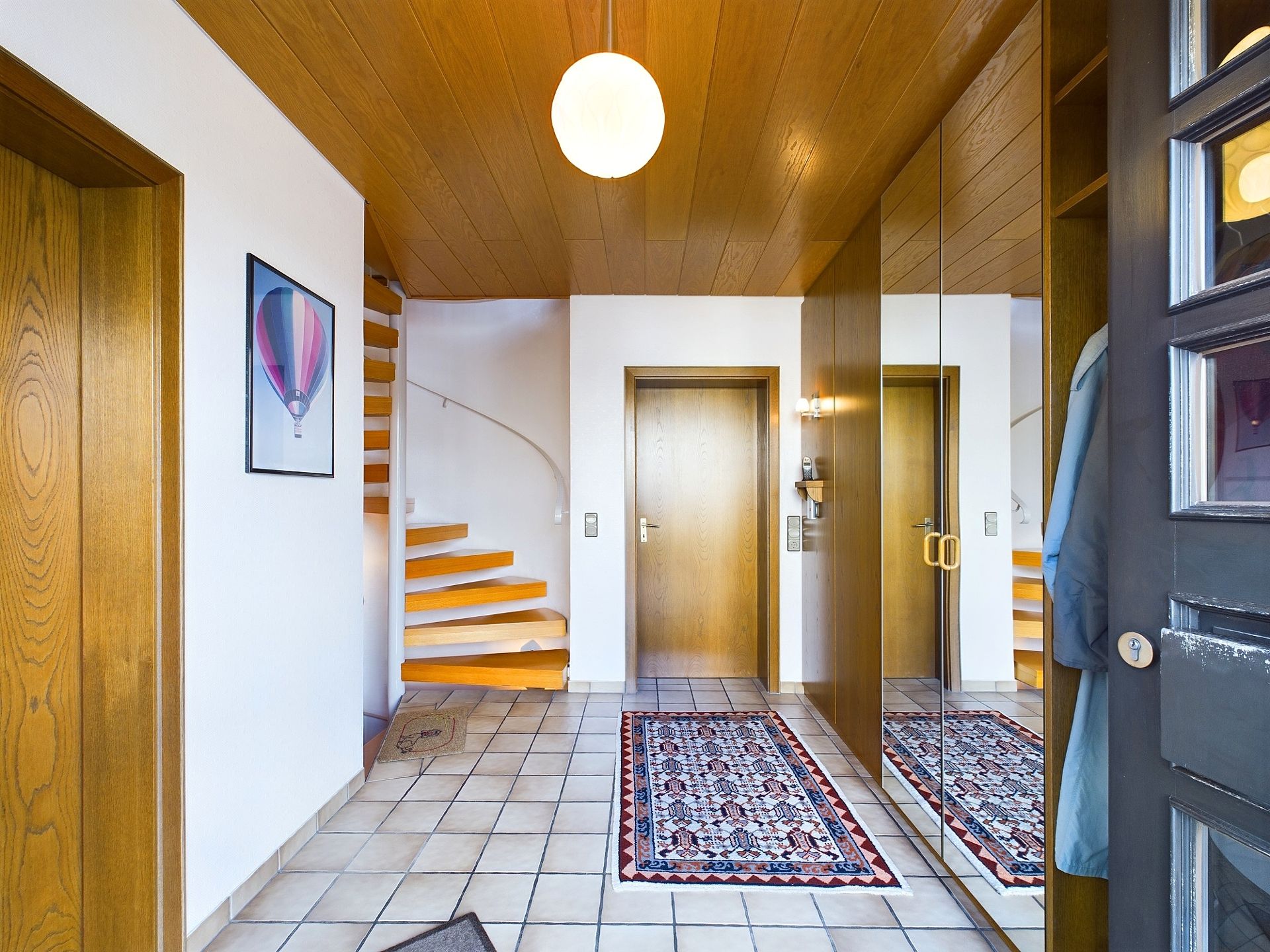 Heller Flur mit Spiegelschrank, Teppichläufer und offener Holztreppe.
