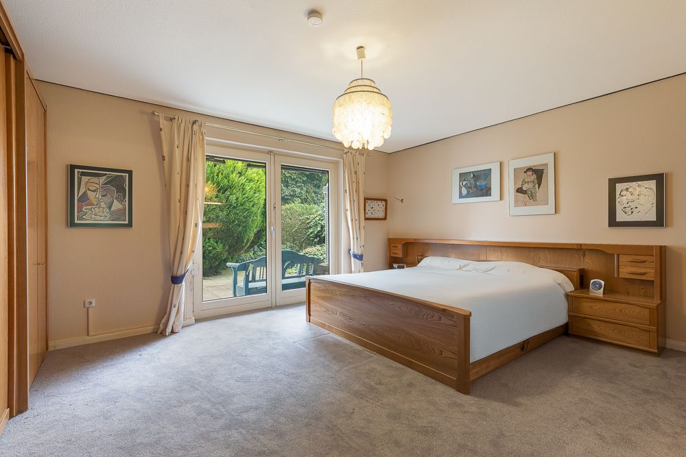 Schlafzimmer mit großem Holzbett, Teppichboden, Wandkunst und Glastür zum Garten.