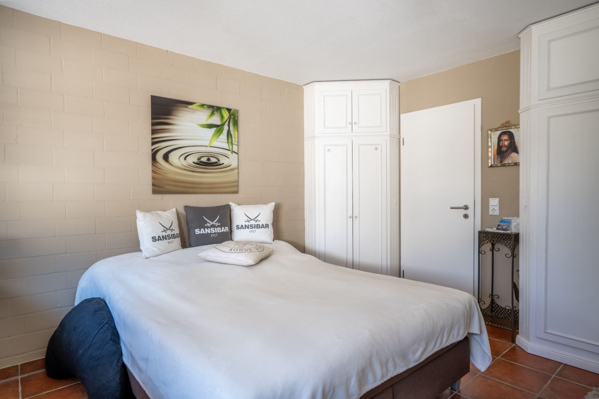 Schlafzimmer mit Doppelbett, weißen Kissen, Wandbild und weißen Einbauschränken.