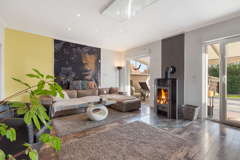 Modernes Wohnzimmer mit Ecksofa, Kaminofen, großem Wandbild und Zugang zur Terrasse.