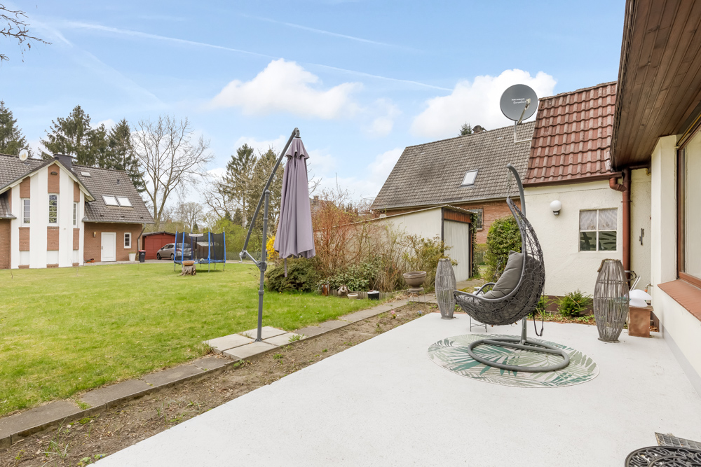 Garten mit Terrasse, Hängestuhl, Sonnenschirm und Blick auf benachbarte Häuser.