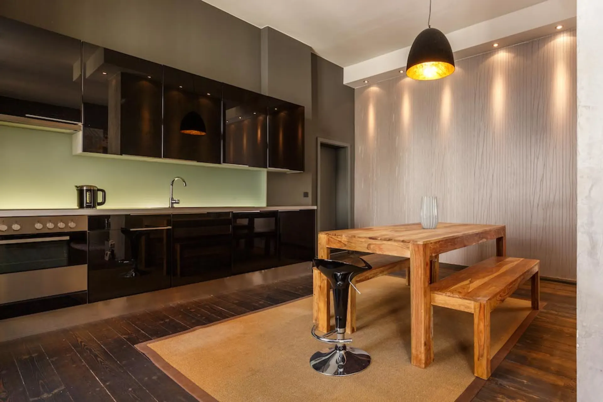 Moderne Küche mit Holztisch, zwei Bänken und einem schwarzen Hocker auf einem Teppich.