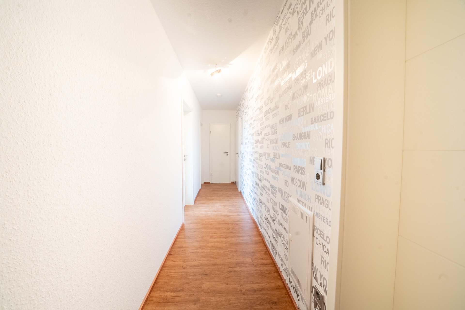 Heller Flur mit Holzboden, weißer Wand und einer Wand mit Städtenamen als Muster.