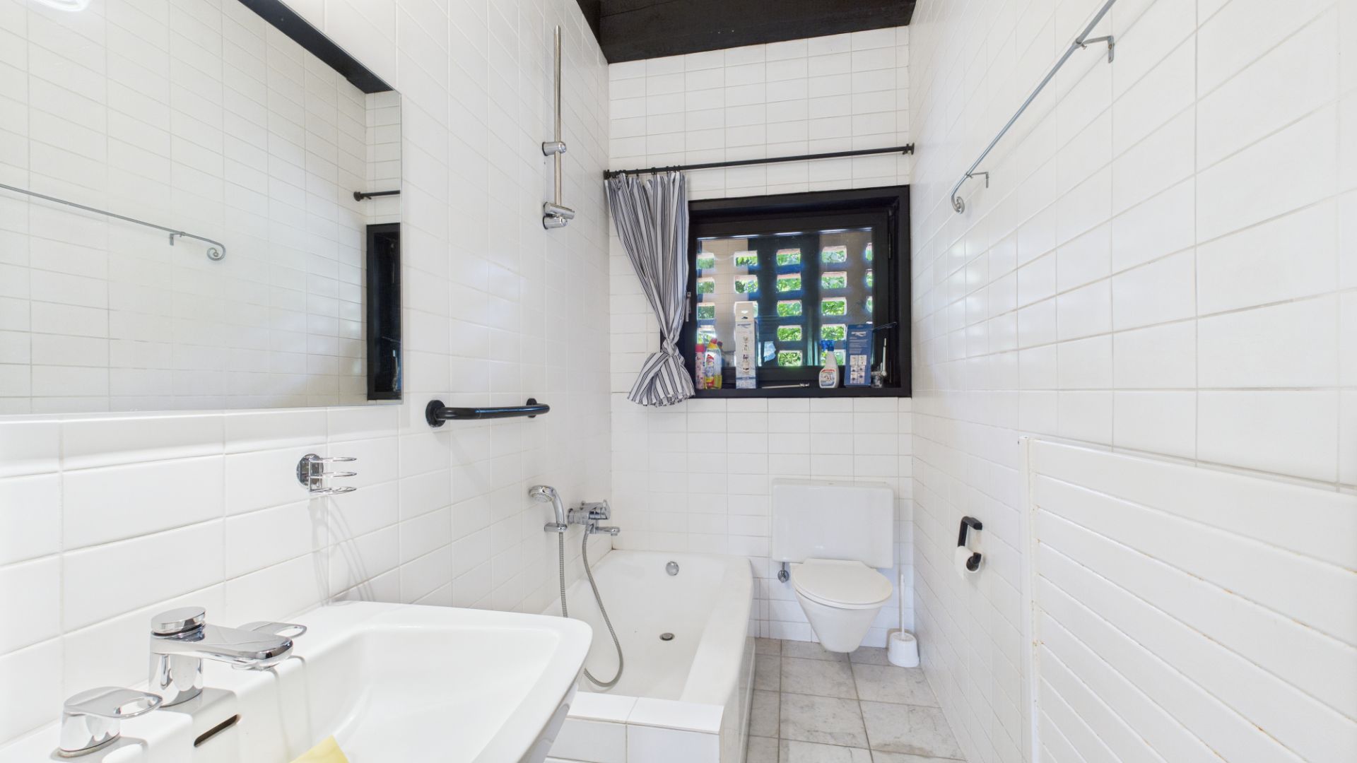 Helles Bad mit Badewanne, Waschbecken, WC und Fenster mit Vorhang.