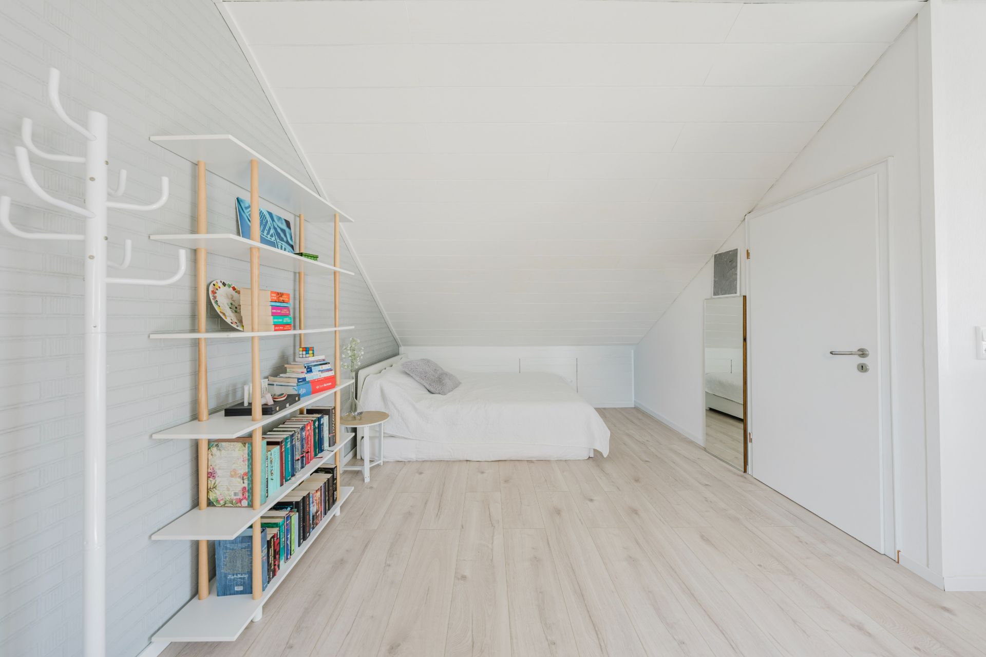 Helles Schlafzimmer mit Bücherregal, Bett, weißer Wand und Dachschräge.