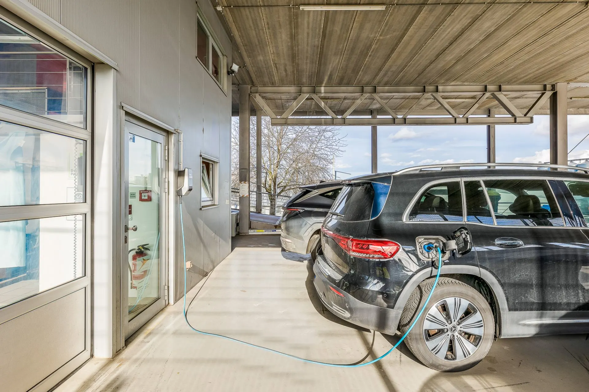 Ein schwarzes Auto lädt an einer Ladestation in einer überdachten Einfahrt eines Wohnhauses.