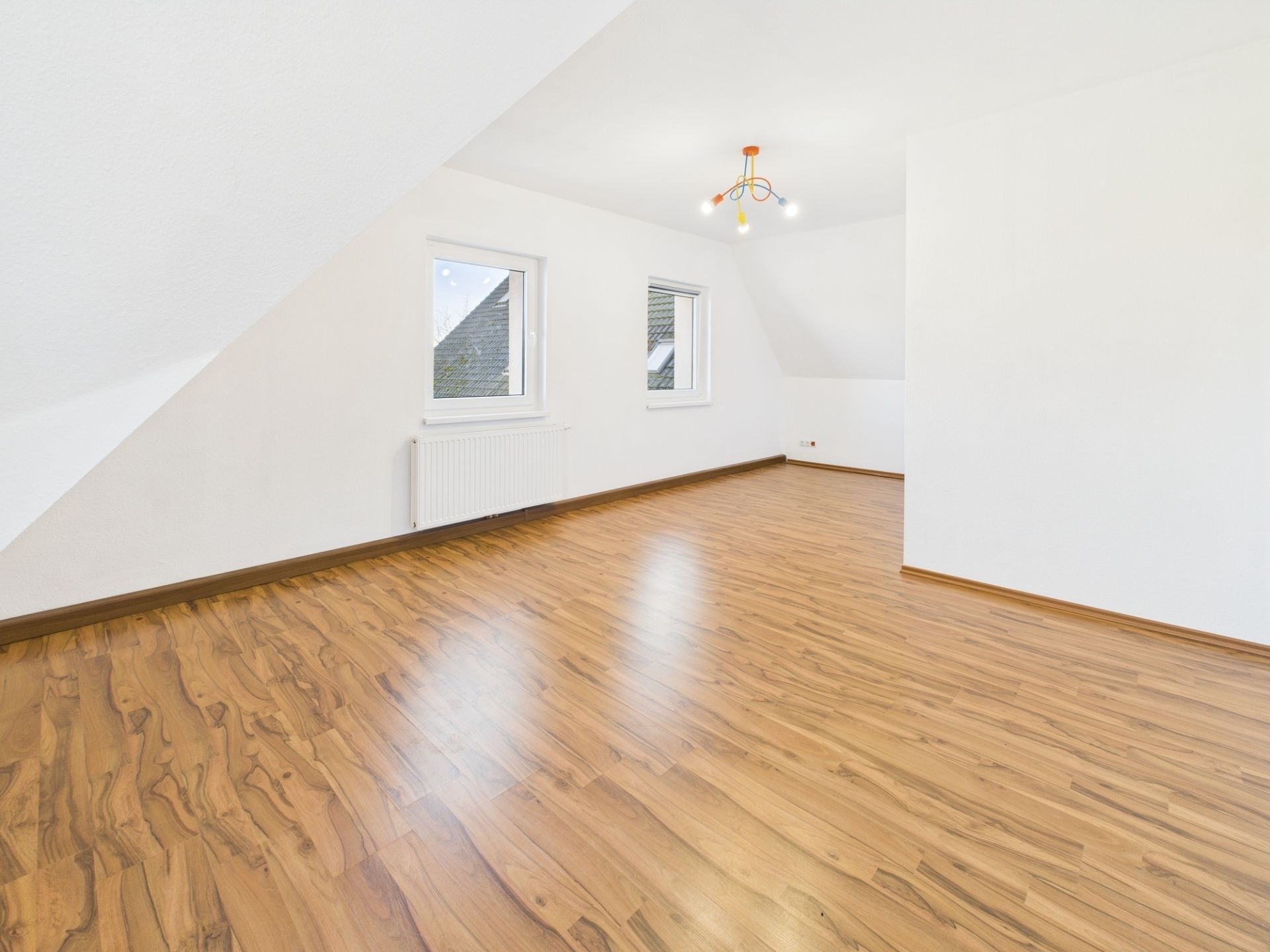 Leerer Raum mit Holzfußboden, zwei Fenstern und weißer Wand.