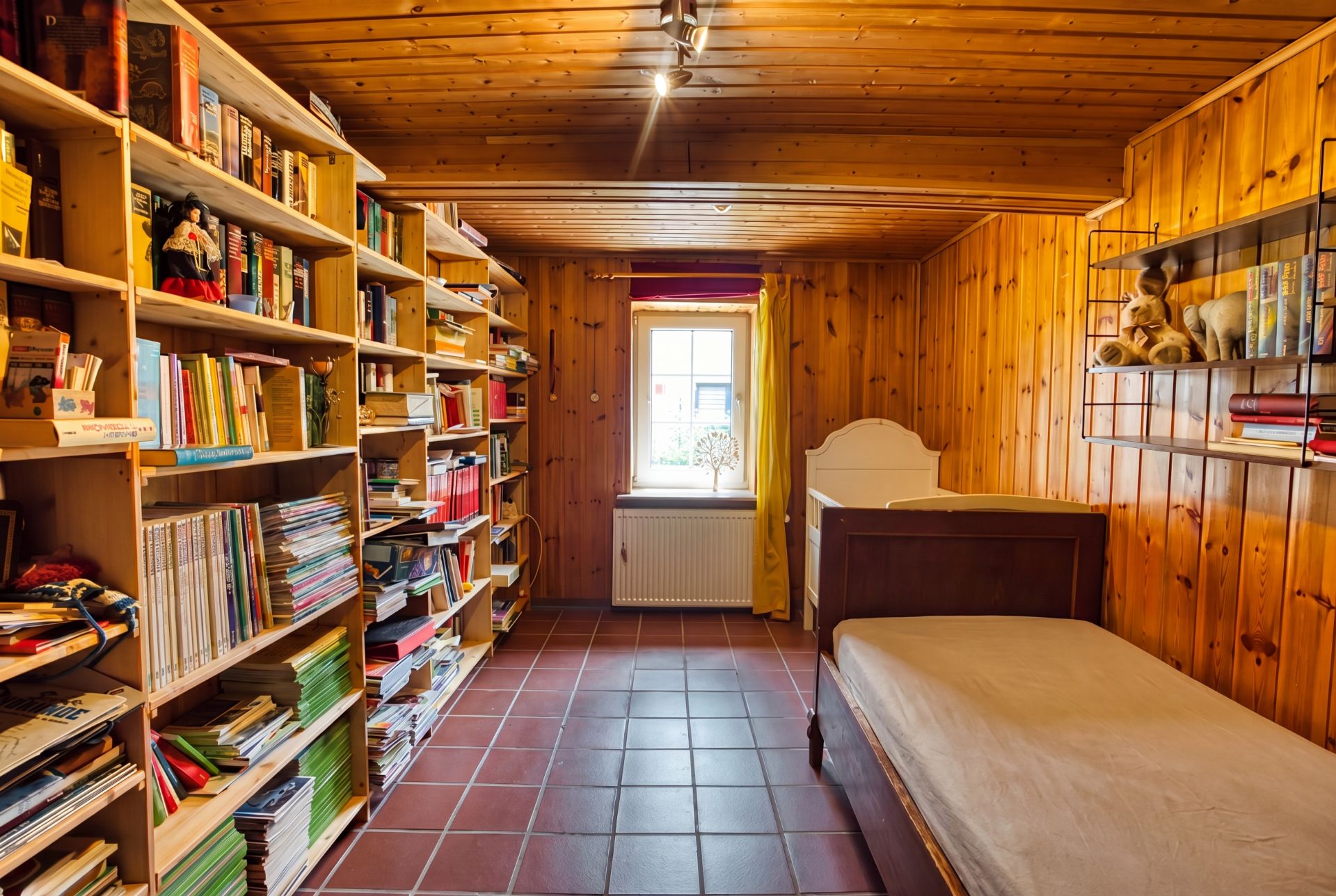 Holzverkleidetes Zimmer mit Bücherregalen, Bett, Fliesenboden und Fenster mit gelben Vorhängen.