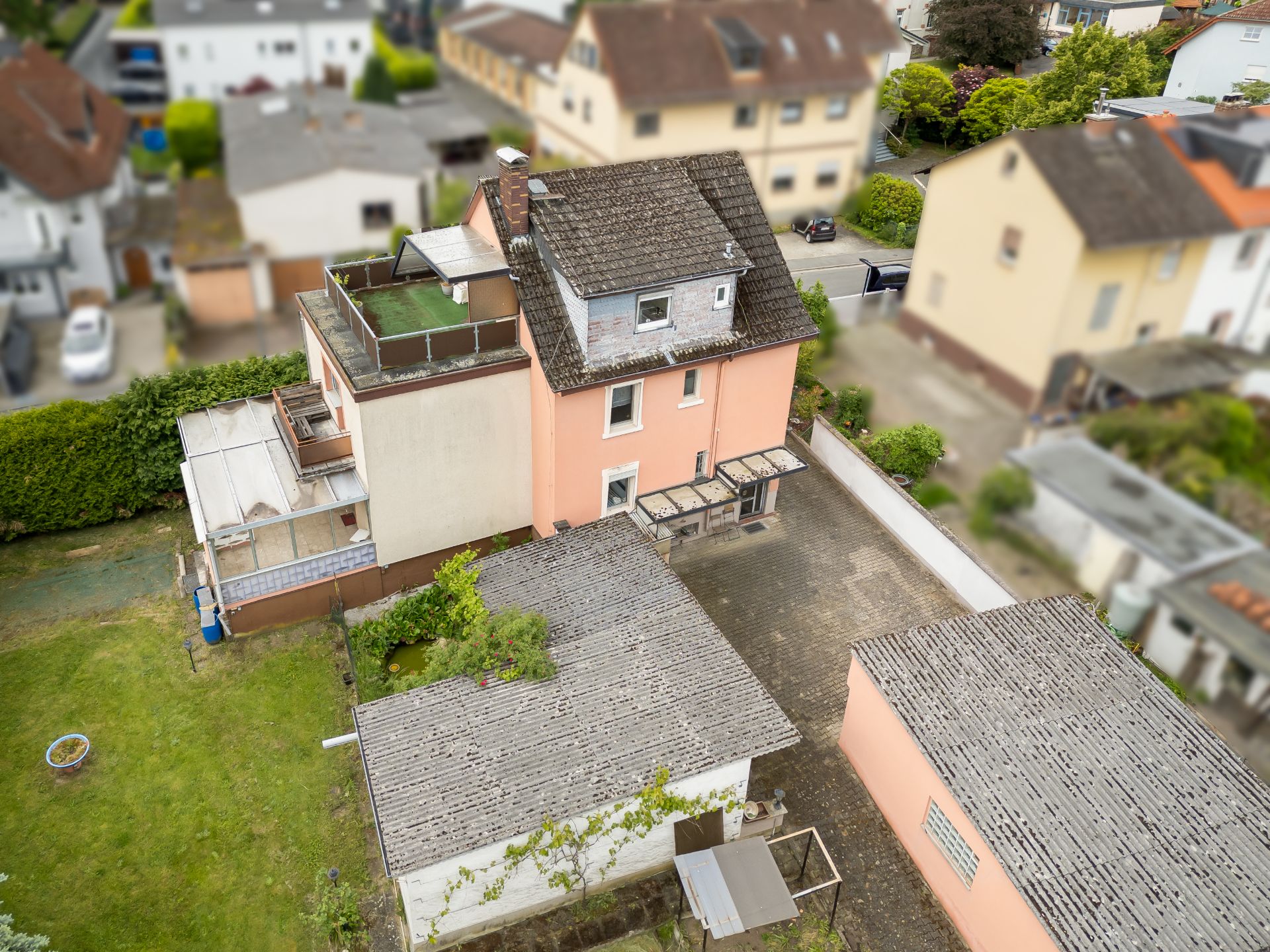 Luftaufnahme eines rosafarbenen Wohnhauses mit Nebengebäuden und Garten.